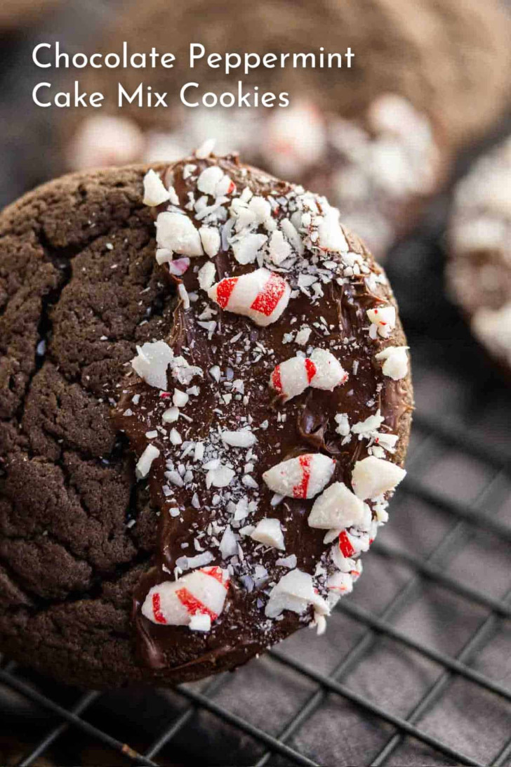A close-up of a chocolate peppermint cookie topped with chocolate icing and crushed peppermint candies, resting on a cooling rack.