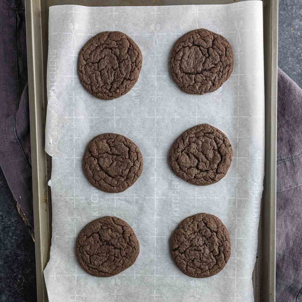 Six chocolate peppermint cake mix cookies are arranged in two columns on a parchment-lined baking sheet.