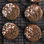 Six chocolate cookies on a cooling rack, each half-dipped in chocolate and sprinkled with crushed peppermint candy—these easy peppermint cake mix cookies are a festive treat for any occasion.