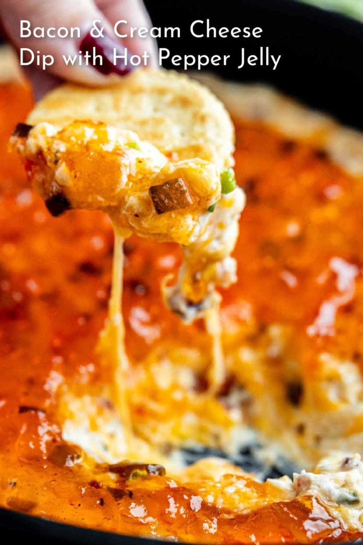 A chip is dipped into a cheesy bacon and cream cheese dip topped with orange hot pepper jelly. The dip is melted and stretchy.