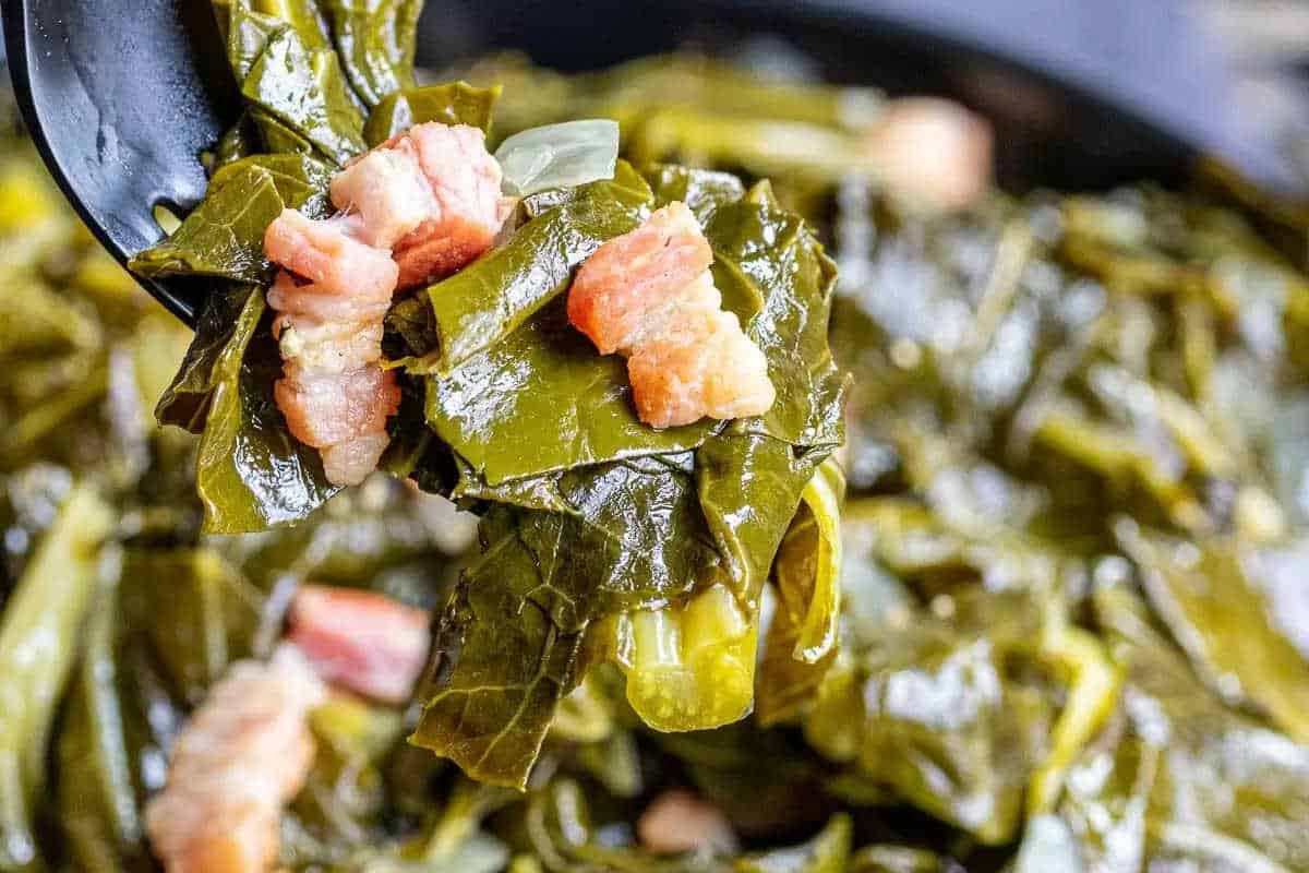 Close-up of cooked collard greens mixed with small pieces of bacon or ham in a pot—a hearty addition to your Ultimate Lineup of Christmas Sides.