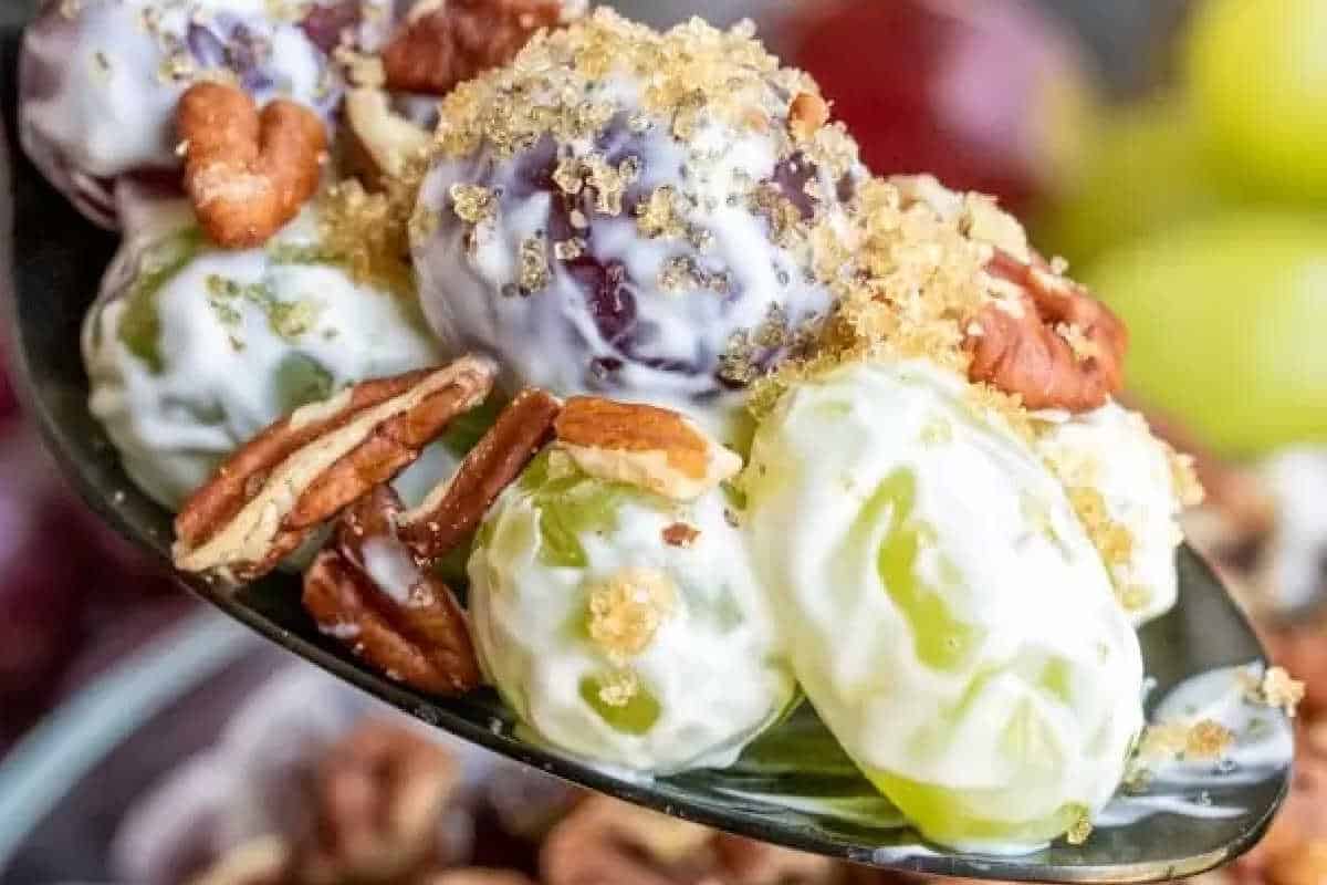 A spoonful of grape salad with both green and red grapes coated in creamy dressing, topped with chopped pecans and brown sugar—an irresistible choice for your perfect plate of Christmas sides.