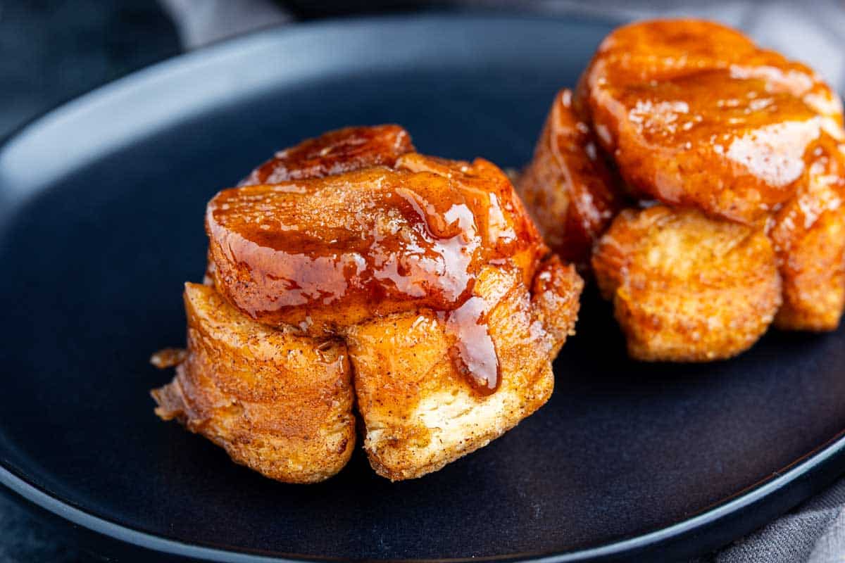 Two sticky, caramel-glazed monkey bread muffins are served on a black plate.