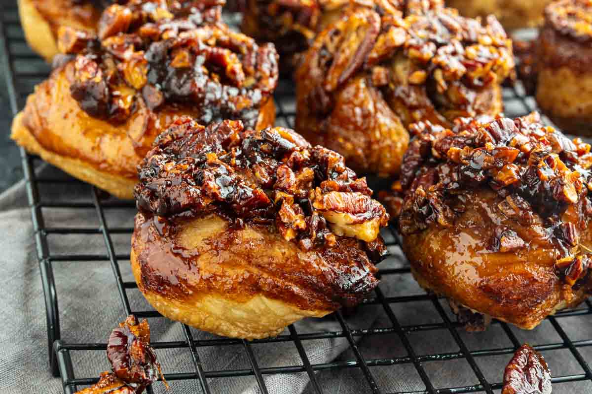 Close-up of sticky buns topped with caramelized pecans and glaze, cooling on a wire rack.