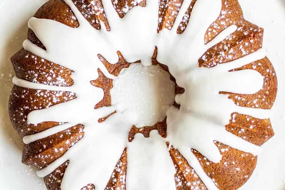 A round bundt cake with white icing drizzled on top and a light dusting of powdered sugar, displayed on a white surface.