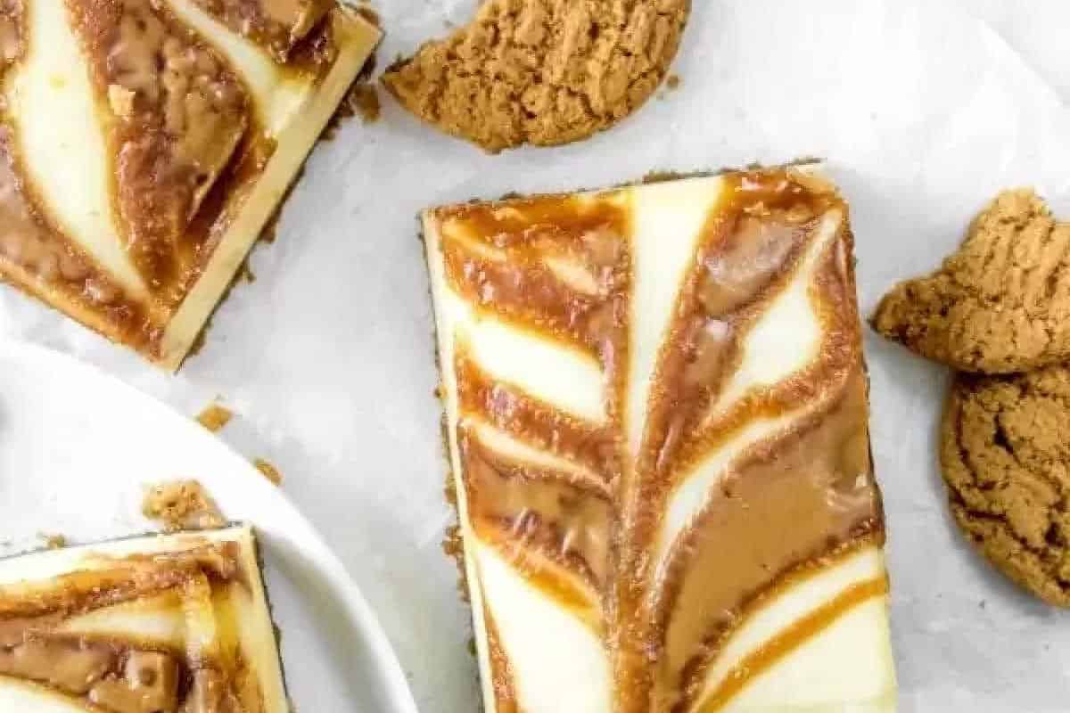 Rectangular cheesecake bars with a caramel or butterscotch swirl on top are arranged next to crumbled oatmeal cookies on a white surface.
