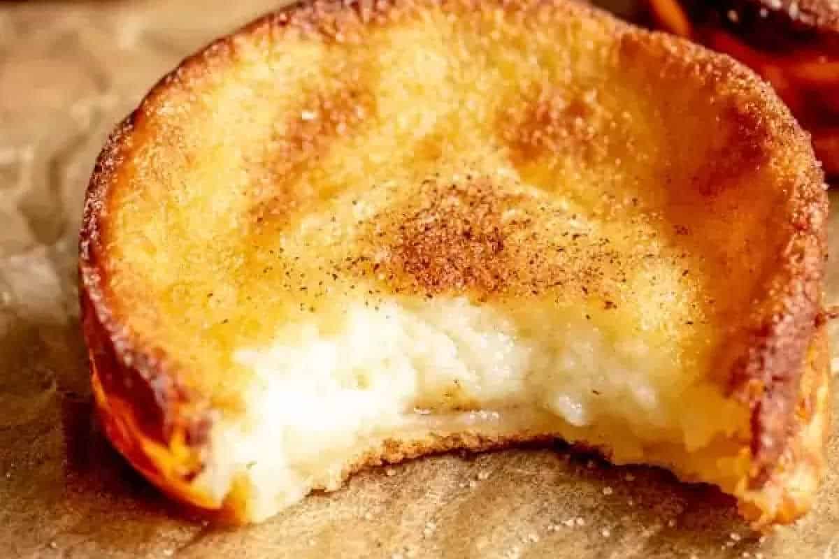 A close-up of a partially eaten custard tart with a golden, slightly burnt crust and creamy filling, sprinkled with cinnamon on top.