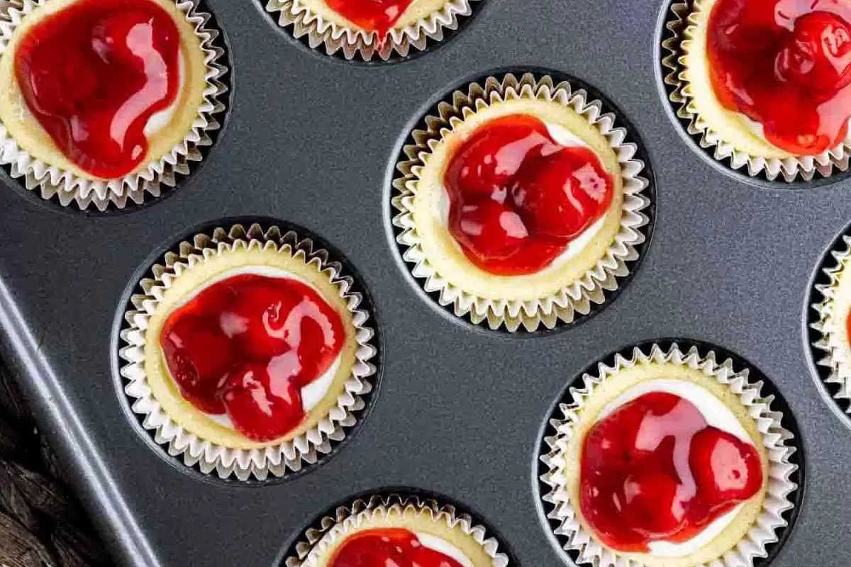 Mini cheesecakes in cupcake liners topped with cherry filling, arranged in a nonstick muffin tin.