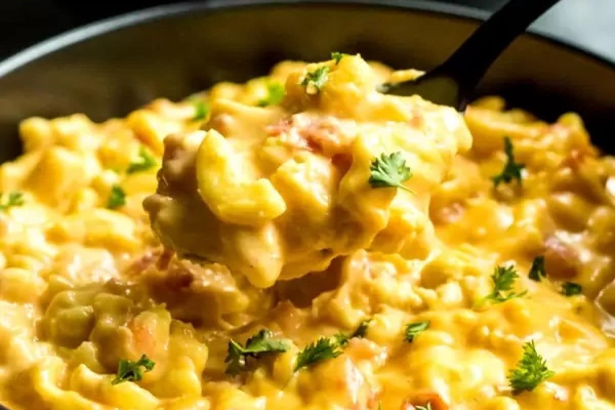 A close-up of creamy macaroni and cheese with chopped herbs sprinkled on top, served in a black bowl.