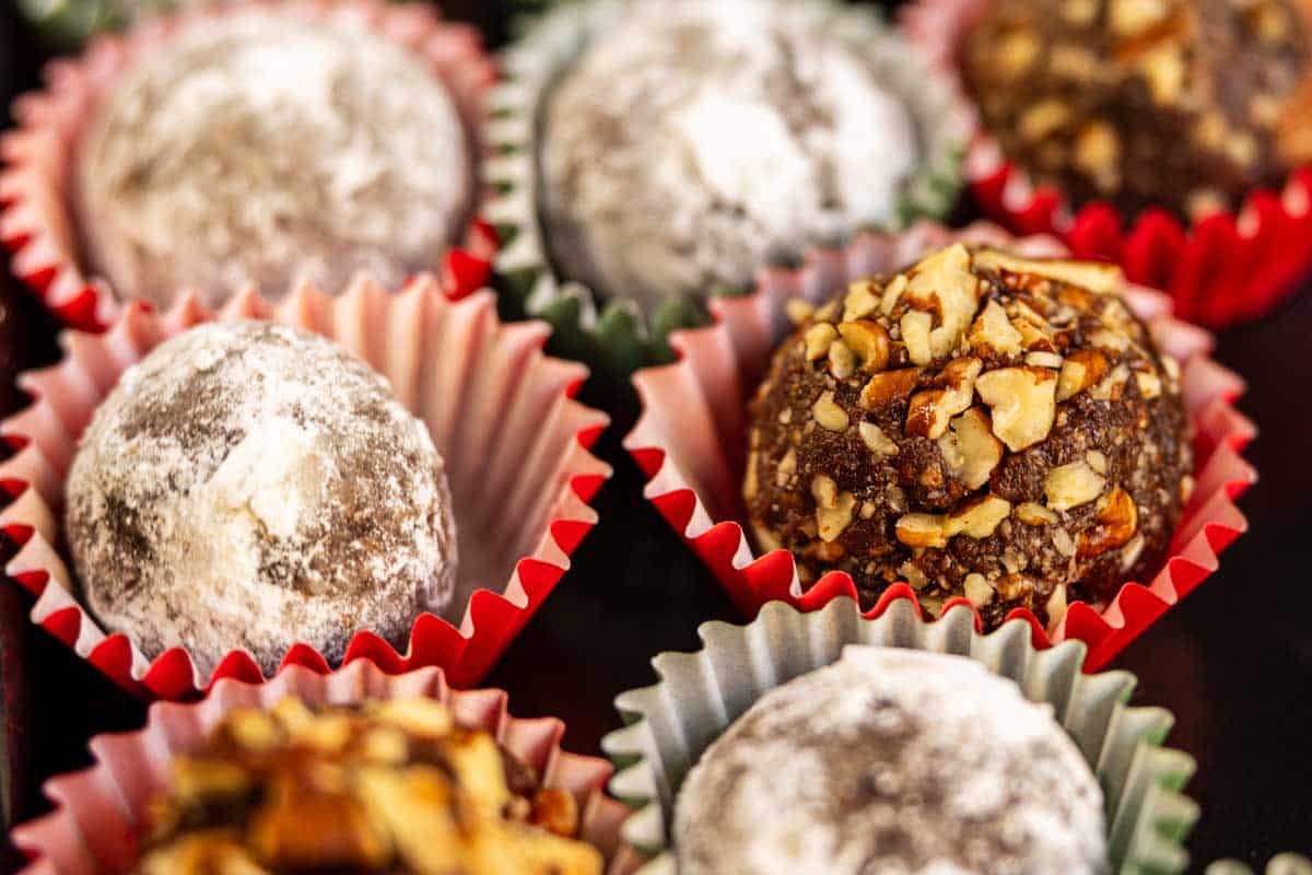 Assorted chocolate truffles in paper wrappers, some coated with powdered sugar and others covered with chopped nuts.
