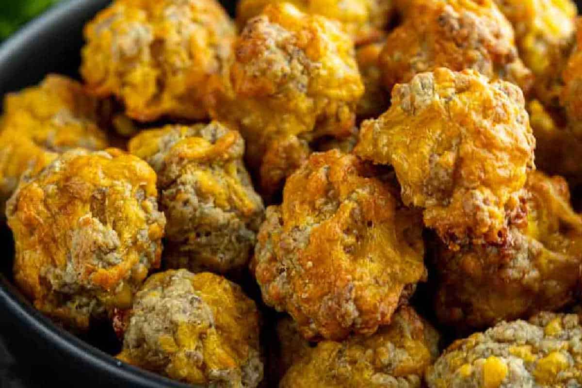 A close-up of a bowl filled with golden-brown baked sausage balls, showing a crispy exterior and bits of sausage and cheese.