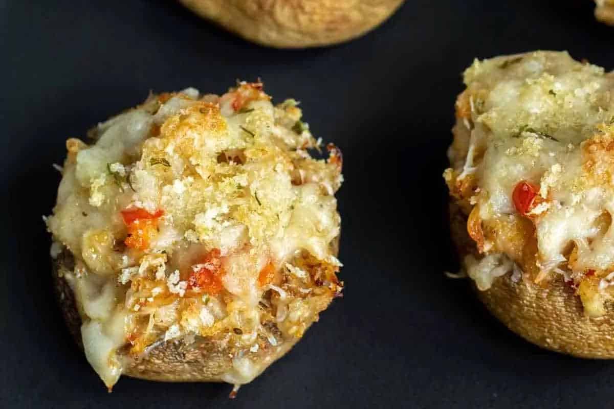 Close-up of stuffed mushrooms topped with melted cheese and breadcrumbs on a dark surface.