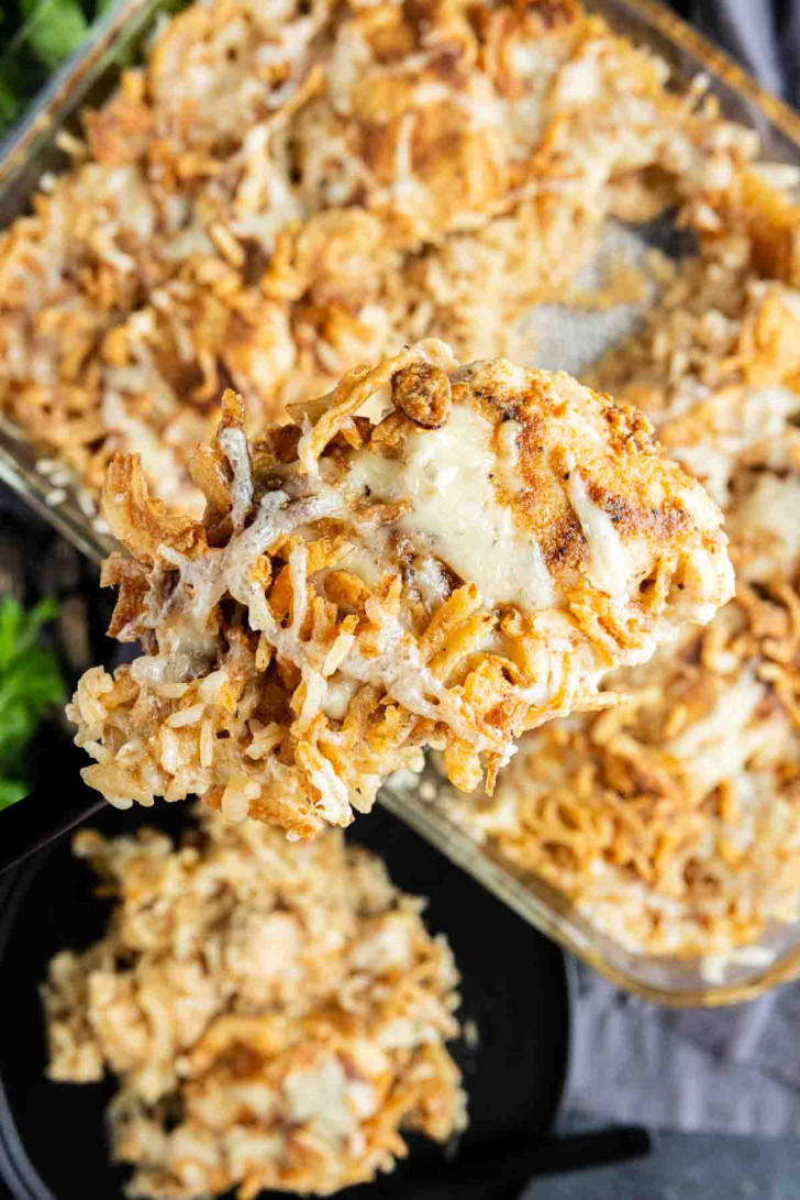 A close-up of a serving of cheesy chicken and rice casserole being lifted from a baking dish, with melted cheese and crispy topping visible.