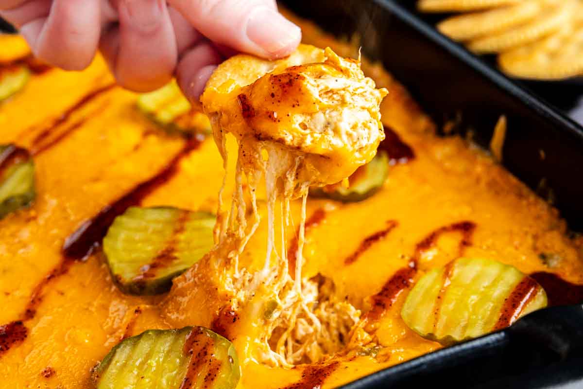 A person holding cheese over a hot chicken dip, perfect for serving as a game day dip.