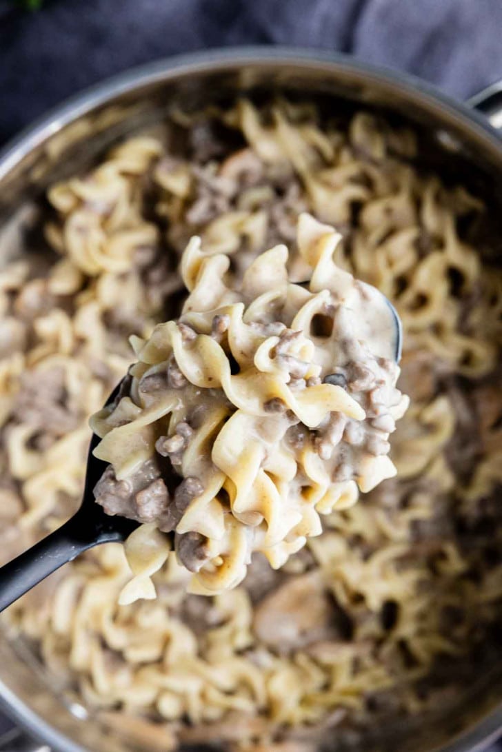 A close-up of a spoonful of creamy beef and noodle stroganoff held over a pot filled with the same dish.