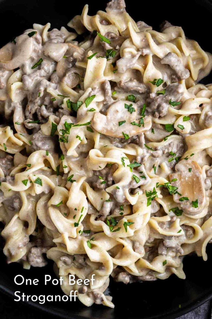 A close-up of one pot beef stroganoff with egg noodles, ground beef, sliced mushrooms, creamy sauce, and chopped parsley on top.