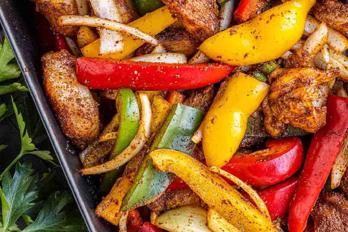 Close-up of a tray filled with seasoned chicken strips, sliced red, yellow, and green bell peppers, and onions—a perfect choice for high-protein recipes to kick off your new year recipes collection.