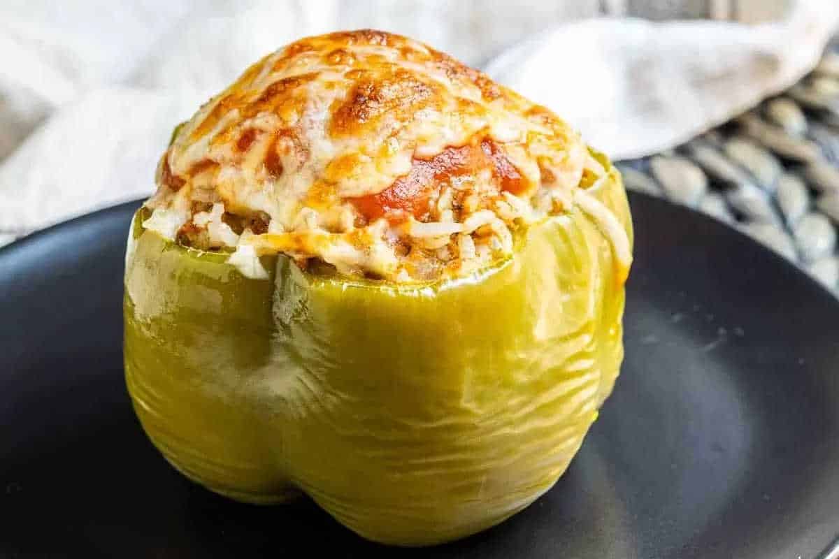 A cooked green bell pepper stuffed with a high-protein meat and rice mixture, topped with melted cheese, served on a black plate—perfect for trying new year high-protein recipes.