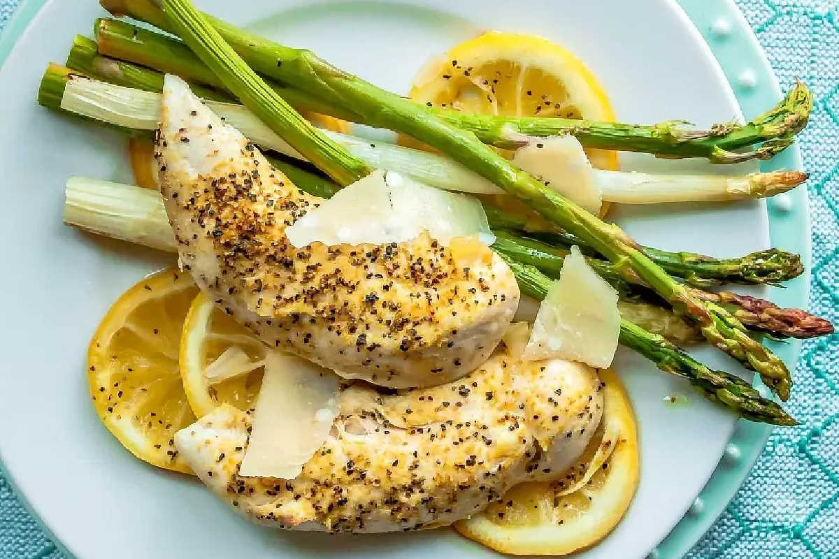 Two pieces of seasoned baked chicken breast served on lemon slices with steamed asparagus and shaved parmesan—a delicious option for best high-protein recipes to start your new year recipes collection.