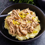 A black bowl filled with mashed potatoes topped with shredded meat and sliced peppers, with a fork on the side.