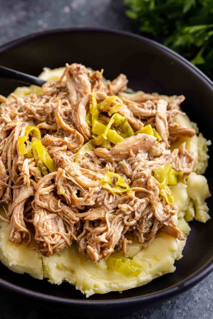 Shredded chicken with sliced peppers served over mashed potatoes in a black bowl.