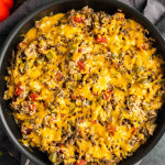 A skillet filled with a mixture of ground beef, rice, diced tomatoes, green peppers, and melted cheddar cheese on top.