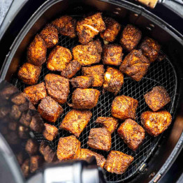 Crispy, seasoned salmon bites cooked in an air fryer basket—perfect for topping a salmon rice bowl or enjoying as a tasty air fryer salmon recipe.