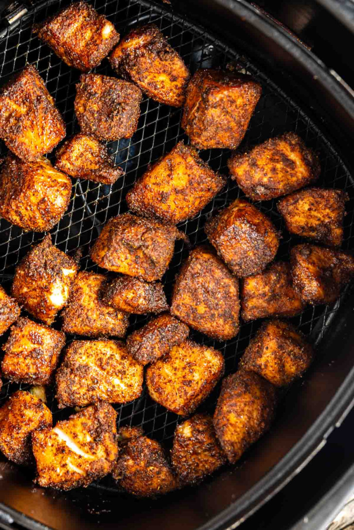 Cubed pieces of seasoned fish are arranged in a single layer inside an air fryer basket, showing a crispy, browned exterior.