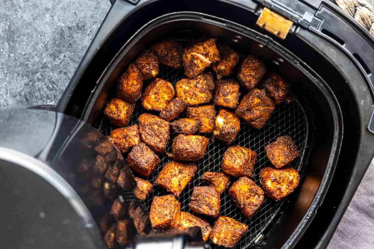 Seasoned chicken pieces cooked in an air fryer basket, viewed from above with the basket partially open—perfect for adding to a crispy rice bowl or as a tasty alternative to your favorite salmon rice bowl.
