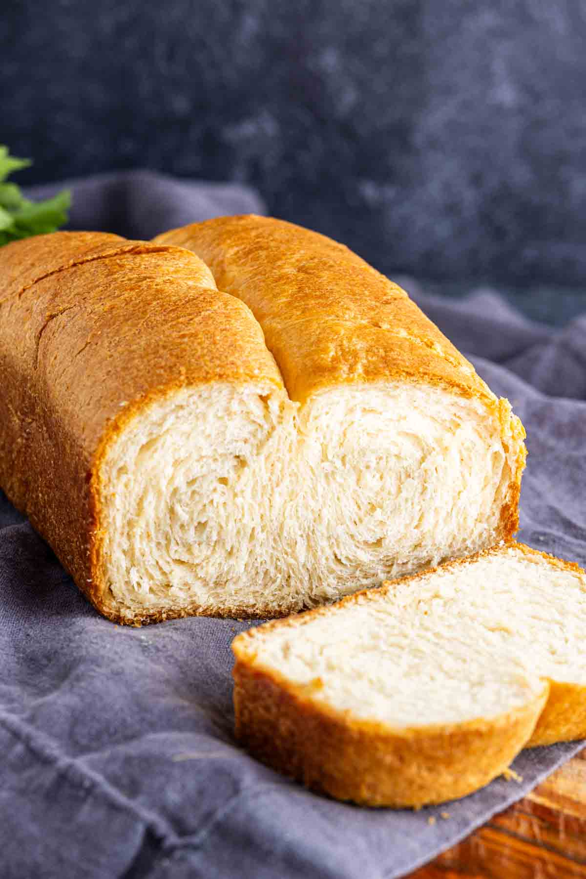 A loaf of freshly baked, buttery bread loaf with a golden brown crust, partially sliced and resting on a gray cloth.
