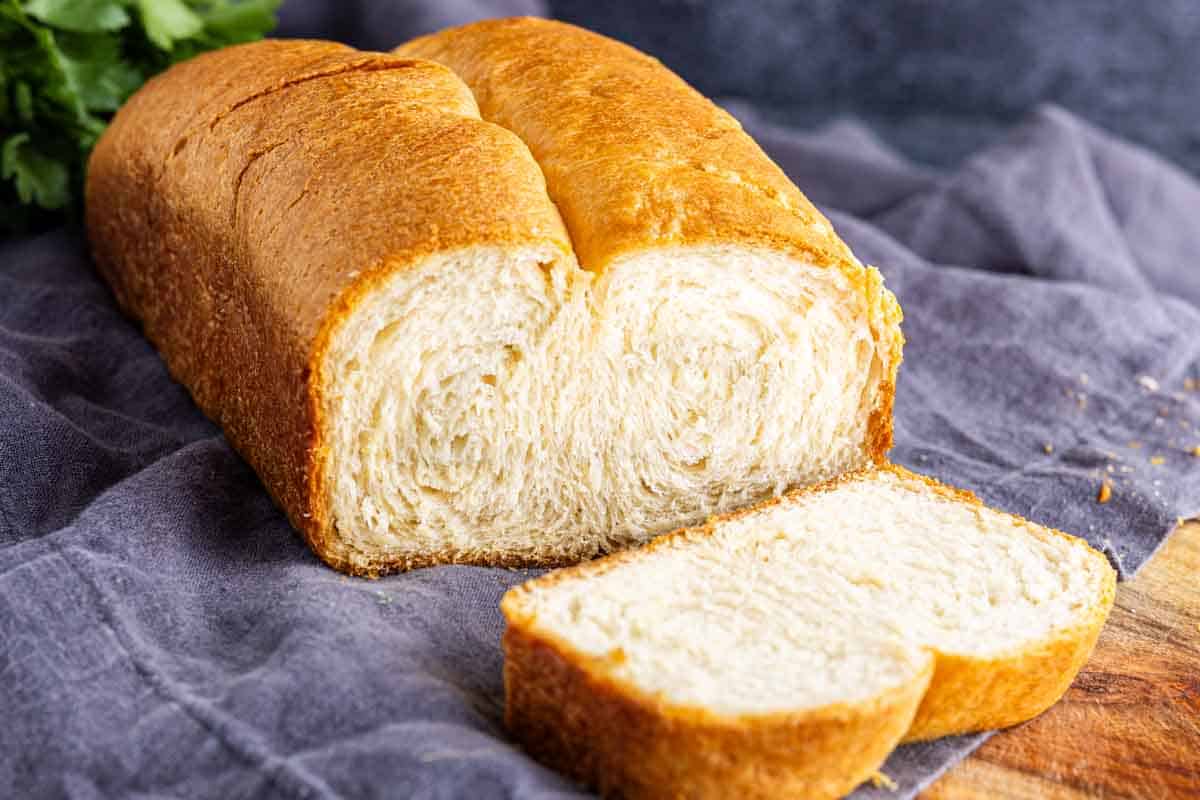 A buttery bread loaf, with two slices cut from it, rests on a cloth and wooden surface—perfect for trying out your latest TikTok bread hack.