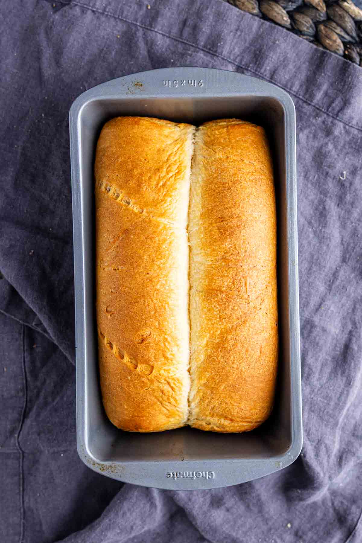 A loaf of golden-brown crescent roll bread in a rectangular metal baking pan, resting on a dark cloth.