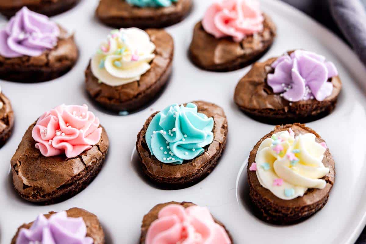 Oval-shaped Easter brownies made from brownie mix dessert, topped with colorful icing and sprinkles, arranged on a white plate.