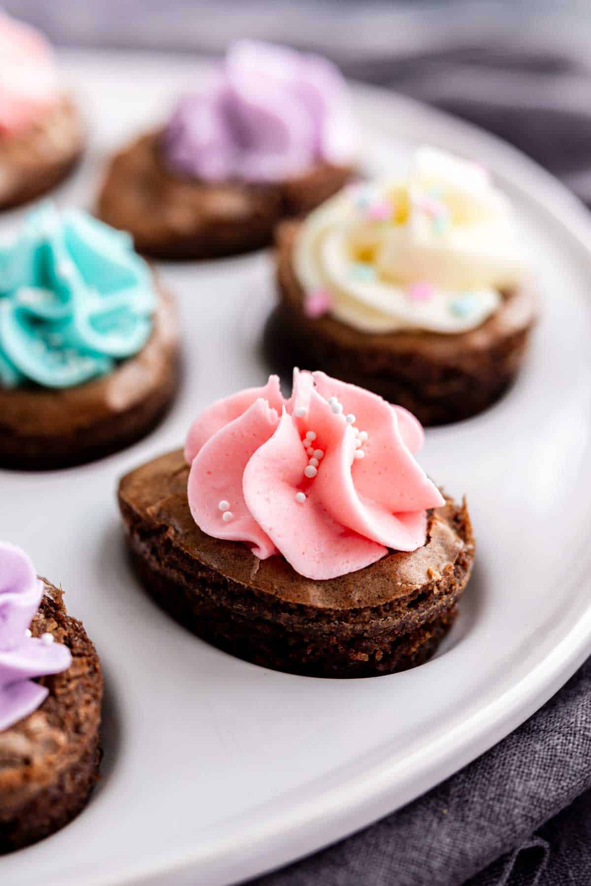 Close-up of heart-shaped Easter brownies topped with colorful swirls of frosting and sprinkles on a white plate—an easy Easter dessert that's as festive as it is delicious.