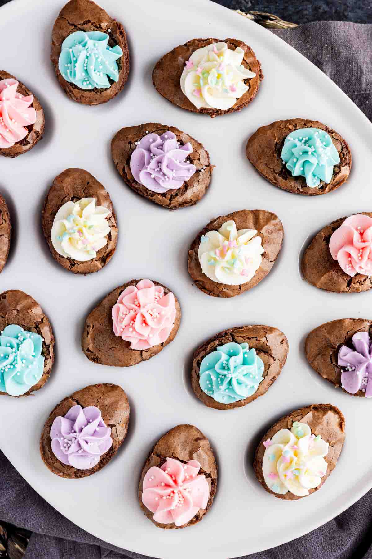 A plate of oval-shaped chocolate cookies topped with colorful pastel icing in pink, blue, purple, and white makes an easy Easter dessert, perfect for celebrating the season.