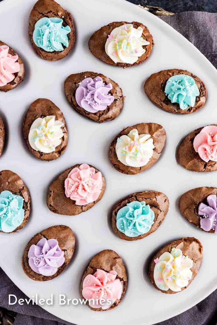 Oval-shaped brownies topped with pastel-colored frosting are arranged on a white plate. The text "Deviled Brownies" appears in the bottom left corner.