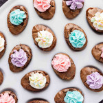 Oval-shaped chocolate cookies topped with pastel-colored flower-shaped frosting are arranged on a white plate.