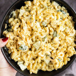 A hand holds a black bowl filled with macaroni salad mixed with diced vegetables and a creamy dressing.