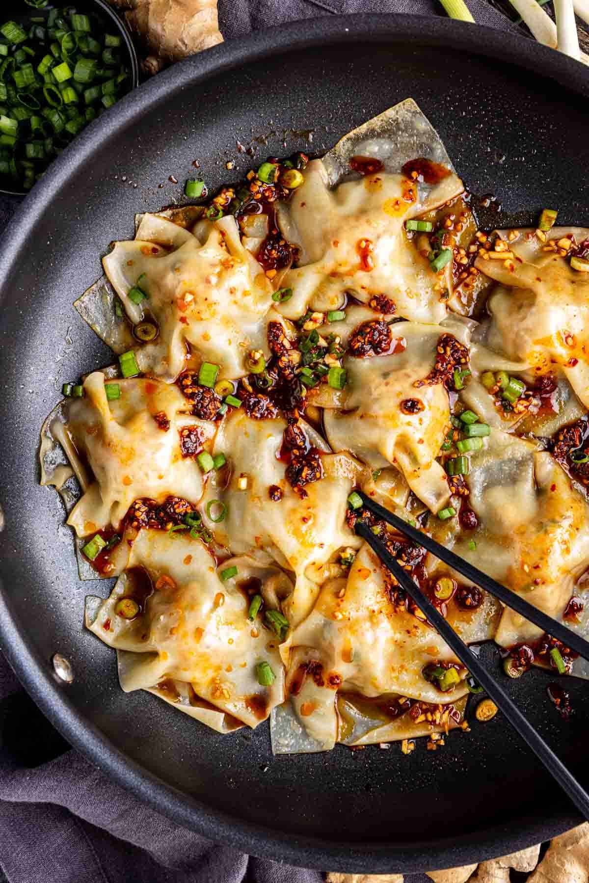 Pan-fried pork dumplings topped with chopped green onions and chili oil, served in a black skillet with chopsticks—these viral blanket dumplings are perfect for sharing.