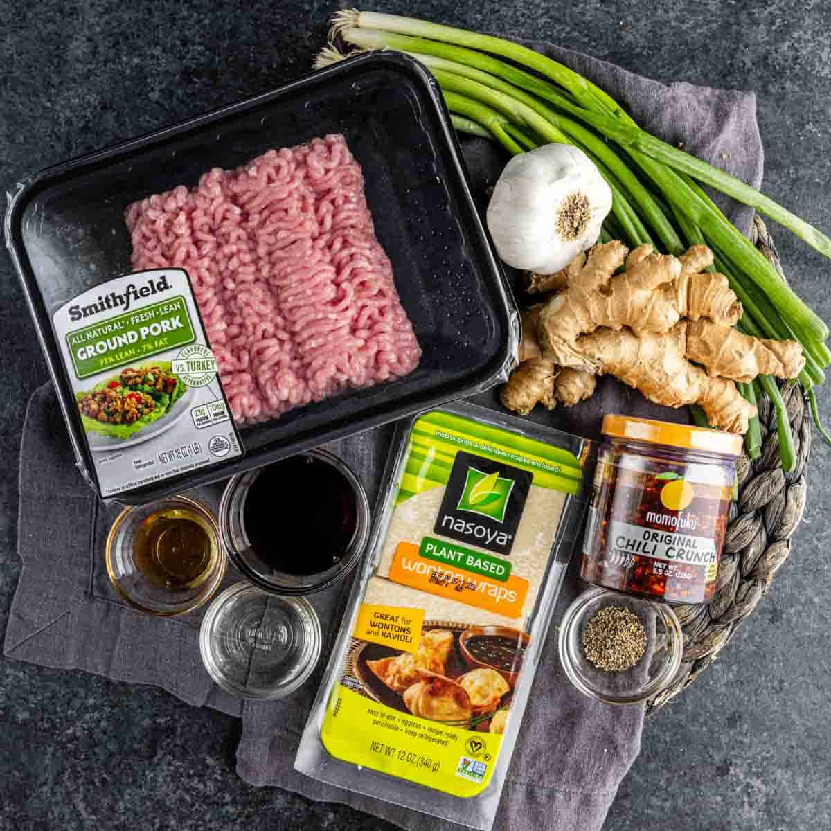 Ingredients for wonton wrapper dumplings, including ground pork, soy sauce, garlic, ginger, green onions, chili crunch, black pepper, and sesame oil, arranged on a dark surface—perfect for creating viral dumpling lasagna.