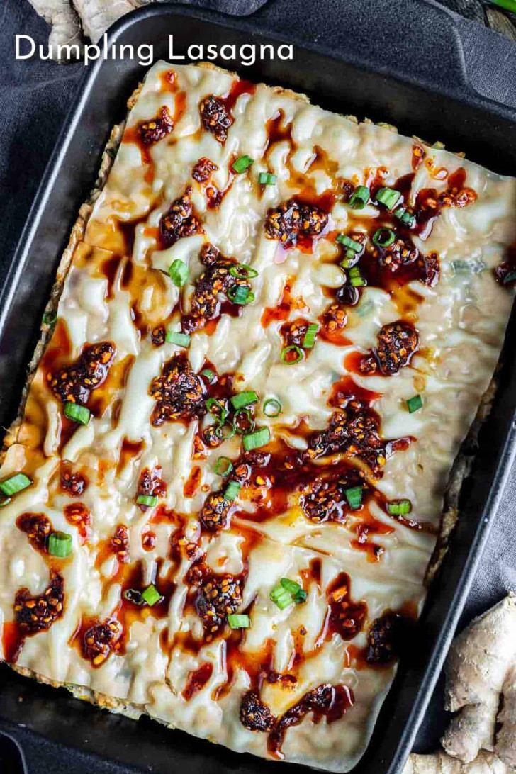 A pan of dumpling lasagna topped with chili sauce, soy sauce, and chopped green onions.