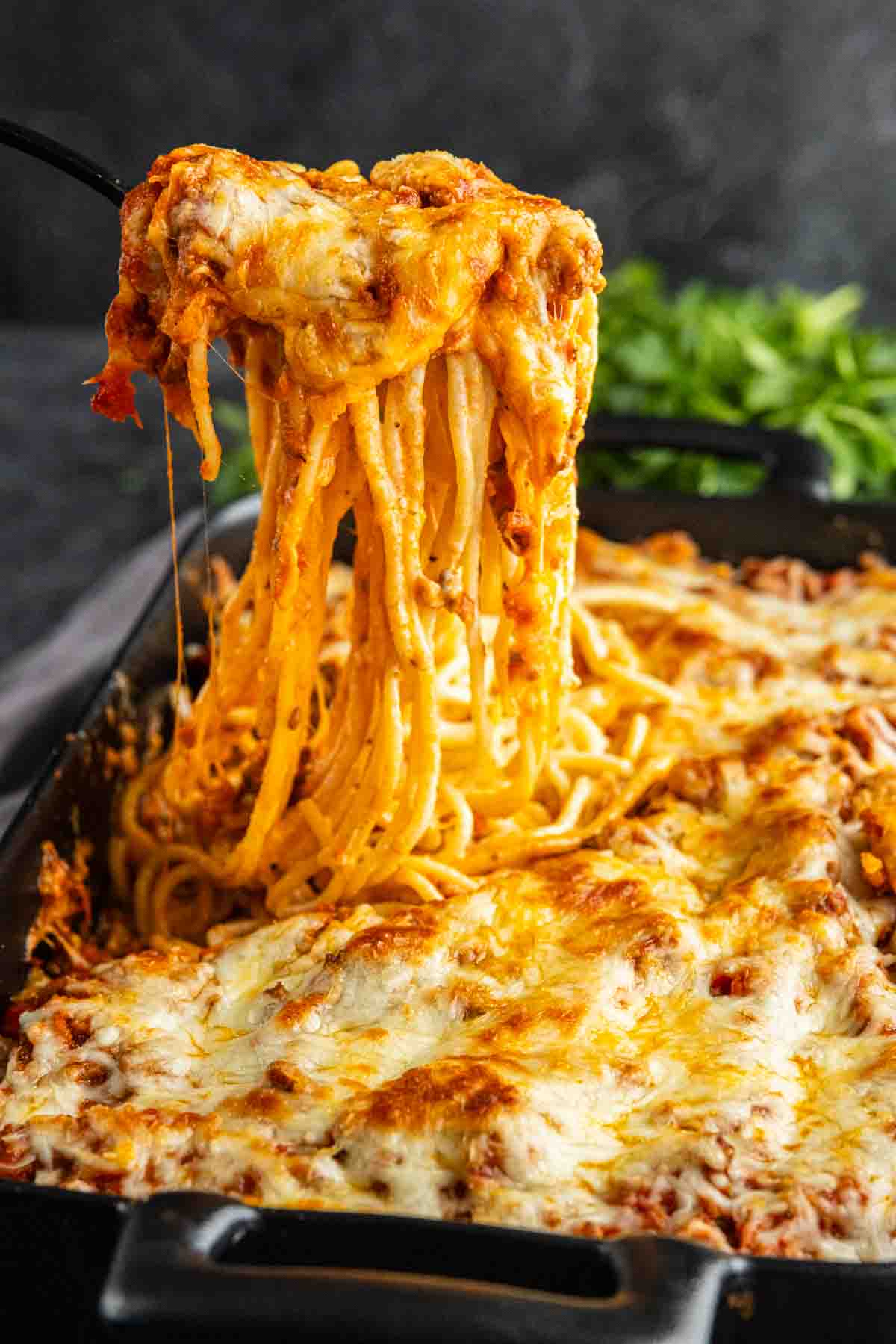 A serving utensil lifts cheesy baked spaghetti from a casserole dish filled with pasta, tomato sauce, and melted cheese.