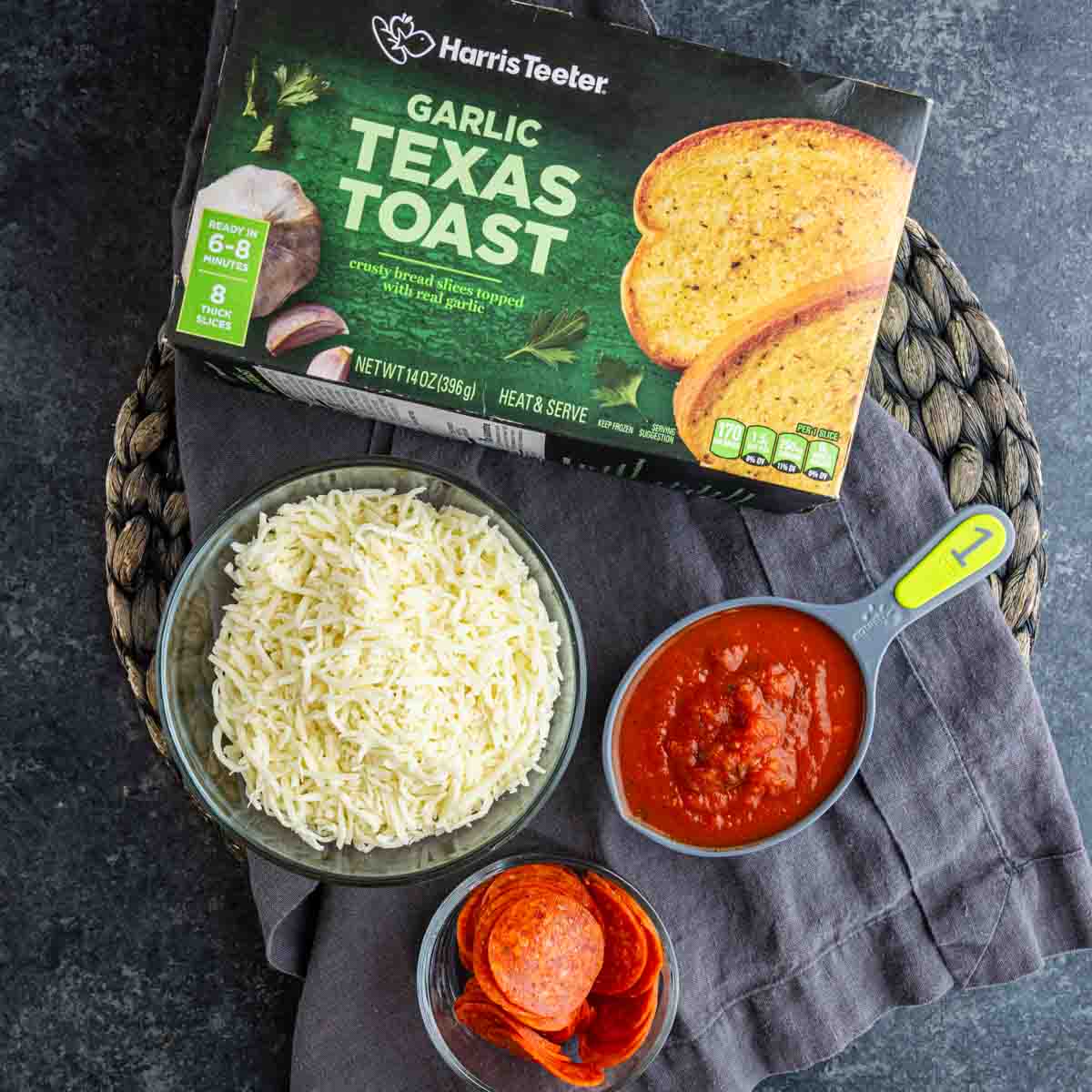 A box of garlic Texas toast, a bowl of shredded cheese, a measuring cup of tomato sauce, and a bowl of pepperoni slices on a dark surface—perfect for making an easy pizza toast recipe like Texas Toast Pizza.