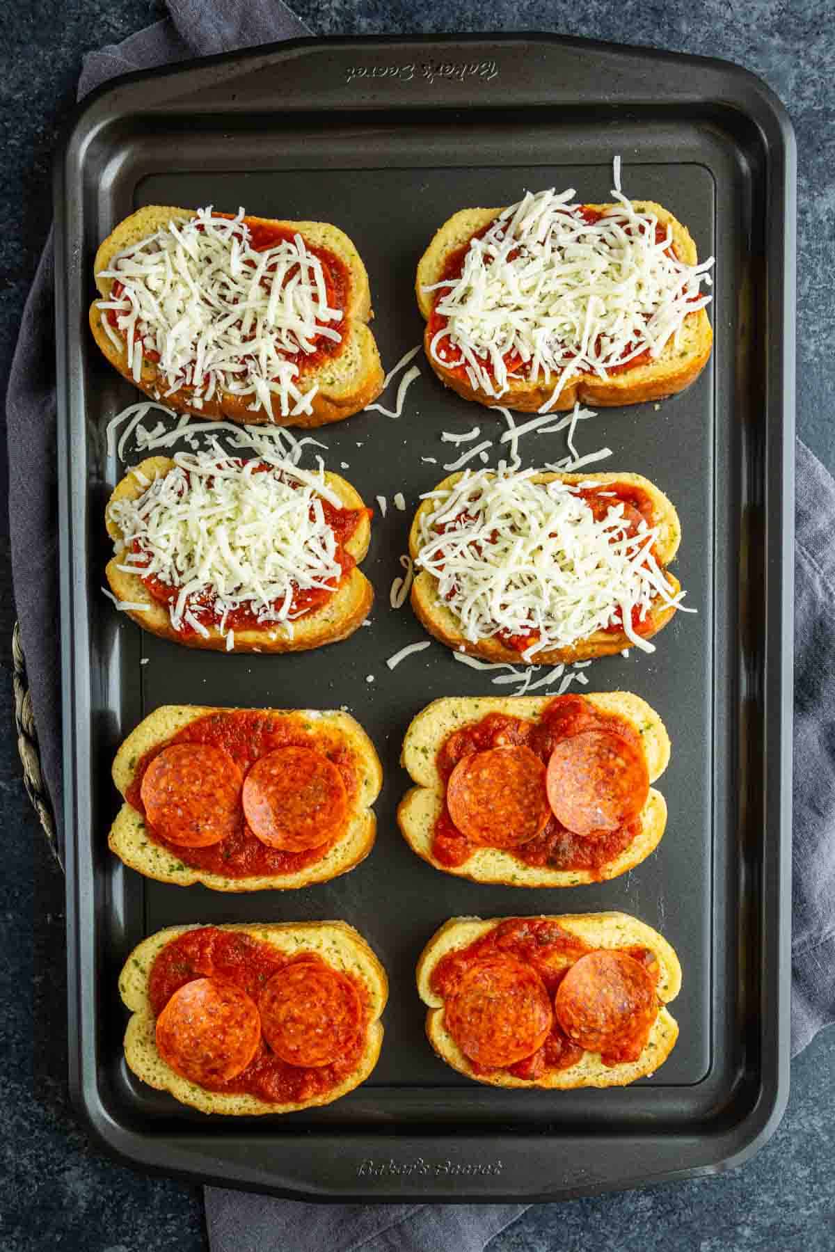 A baking tray with eight pieces of bread; four are Garlic Bread Pizza topped with sauce, cheese, and pepperoni, while four have just sauce and cheese—ready to be baked as easy pizza toast recipe French bread pizzas.