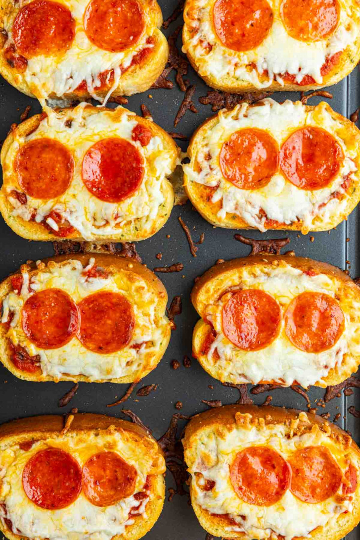 Eight pieces of French bread pizza topped with melted cheese and two slices of pepperoni on each are arranged on a baking sheet.
