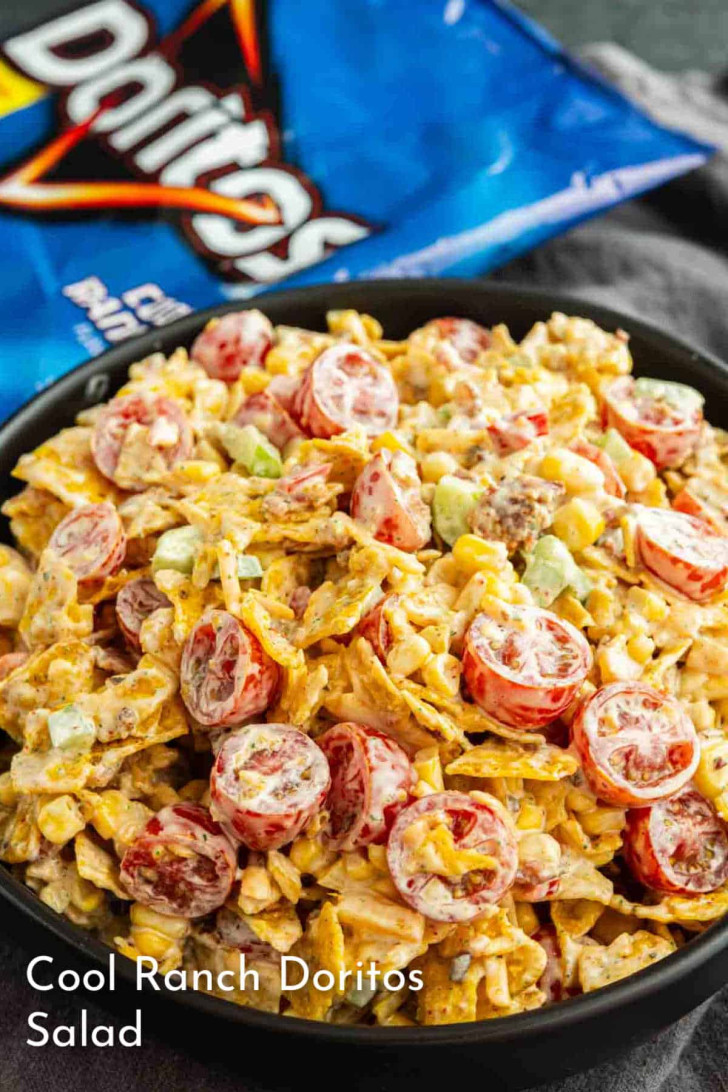 A bowl of Cool Ranch Doritos salad with sliced cherry tomatoes, corn, green onions, and crumbled Doritos, with a bag of Doritos in the background.