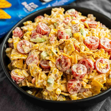 A bowl of Cool Ranch Doritos Salad with cherry tomatoes, corn, celery, cheese, and chips, all tossed in a creamy dressing.