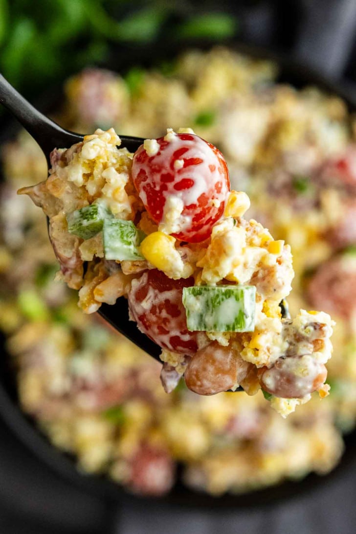A close-up of a spoonful of creamy salad with cherry tomatoes, corn, green peppers, beans, and cheese—perfect as a Southern potluck side dish or for your next summer BBQ side.