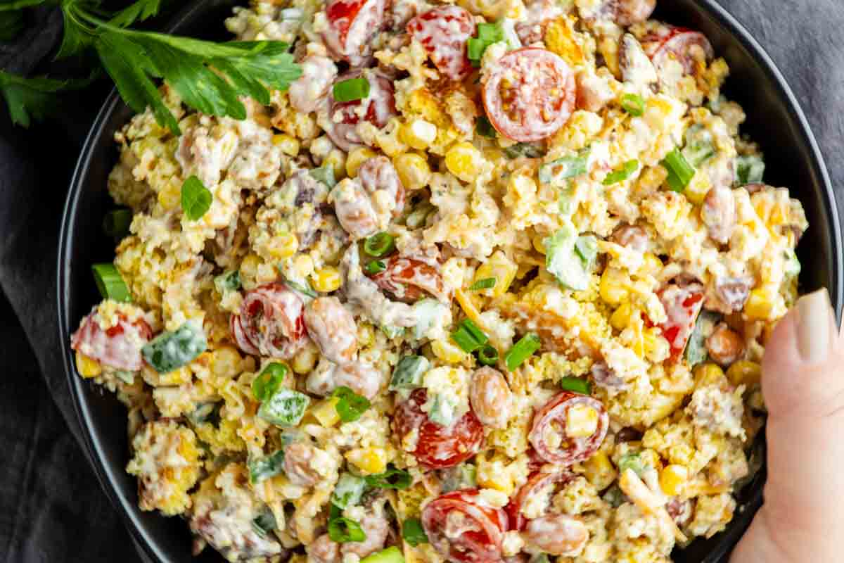 A bowl of salad with corn, cherry tomatoes, beans, green onions, and a creamy dressing, garnished with fresh herbs—perfect as a summer BBQ side or classic Southern potluck side dish.