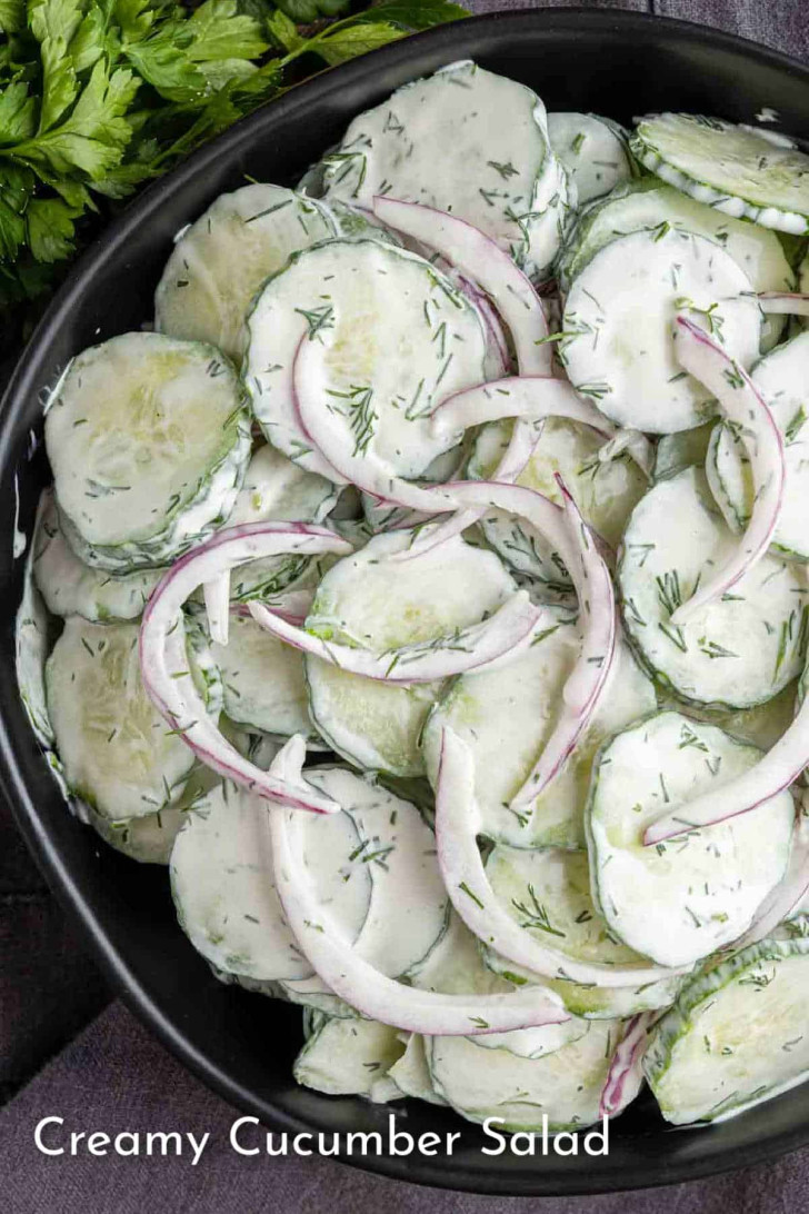 A bowl of creamy cucumber salad with sliced cucumbers, red onion, and herbs, coated in a white dressing.
